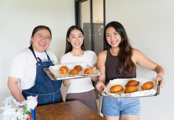 Three women laughing and posing with trays of shio pan buns made with flavoured butter during hands-on workshops in Singapore