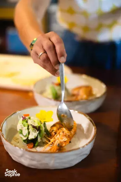 Serving spoon lifts a plated Thai-style dish with fresh herbs at a Chiang Mai cooking class in The Farmer's Lab chef’s table