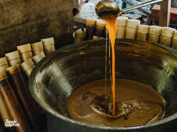 Golden palm sugar syrup poured from a ladle into a large cauldron during a Tanoti Crafts workshop in Kuching