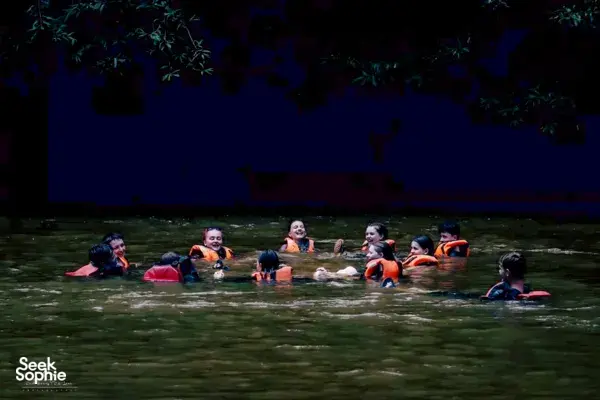 Snorkellers wearing orange life vests floating in a dark river at dusk surrounded by trees in Malaysia