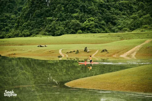 Aerial view of a small orange boat crossing a calm green lake through open valley scenery on the Cao Bang motorbike loop