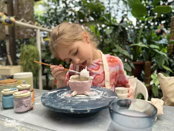 Young child carefully painting a small ceramic piece at an outdoor table in Tiong Bahru pottery studio, one of Singapore hidden gems