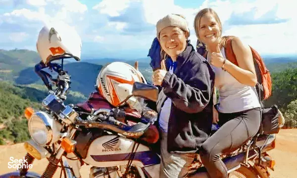 Smiling travellers pose with a Honda motorbike on a scenic mountain road near Da Lat during an Easy Rider to Mui Ne