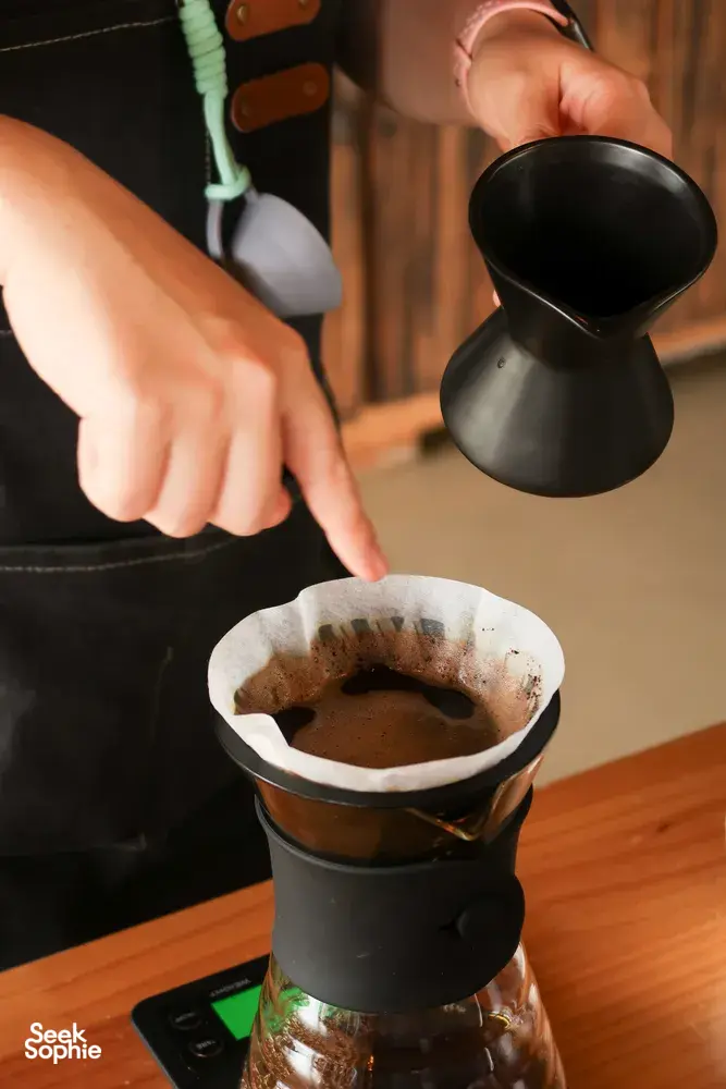 Hand pours hot coffee into a paper filter over a carafe while brewing at a specialty coffee workshop in Lijiang