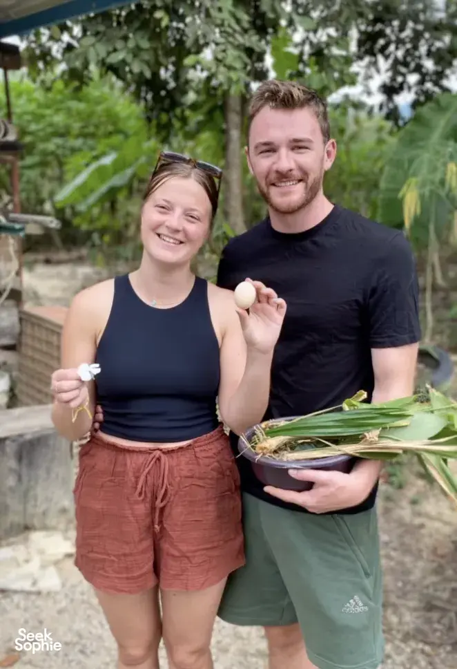 Kebun Lidstari hosts smiling outdoors in Langkawi, holding green leaves and a basket of herbs from the garden