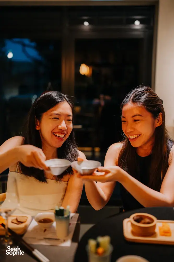 Friends sharing a sake tasting in a cosy Singapore shop, smiling as they raise small cups—at SakeMama