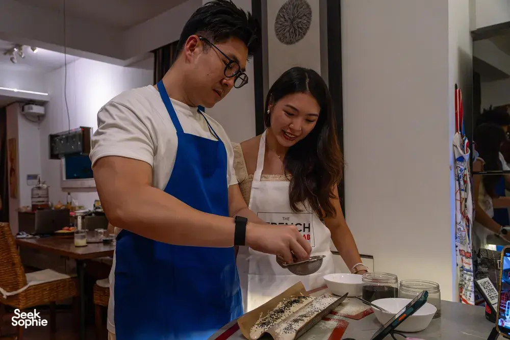 Host-led kitchen session: two people preparing food on a counter in a cosy Singapore loft, private dining Singapore