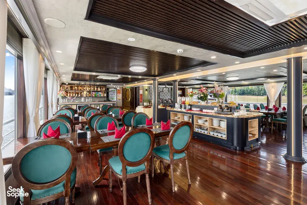 Bar lounge on the Oasis Bay Party Cruiser with teal upholstered chairs and a central drink counter for socialising in Halong Bay