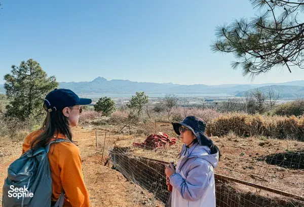 Hikers pausing on a rural trail with mountains in the distance near Lijiang during a Yi & Naxi village trek