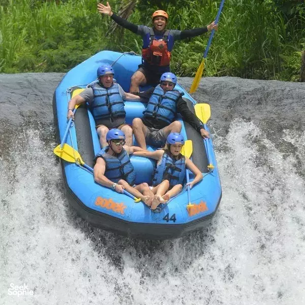 Helmed rafters in a blue inflatable raft cheering through steep rapids on a forest river in Indonesia