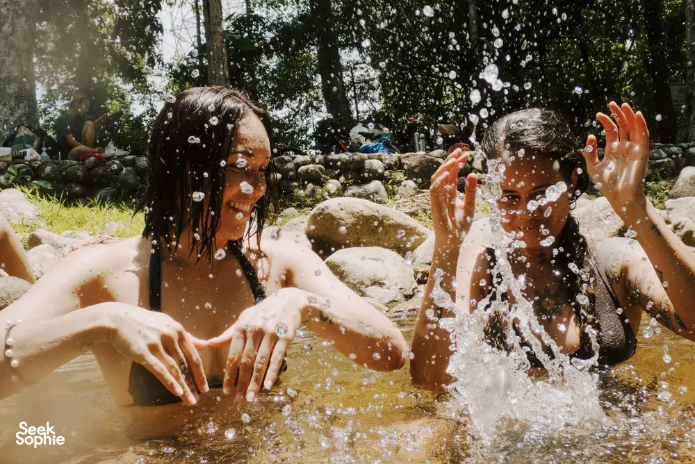 People laughing and splashing in a shallow jungle pool on a Langkawi nature stop, surrounded by rocks and greenery
