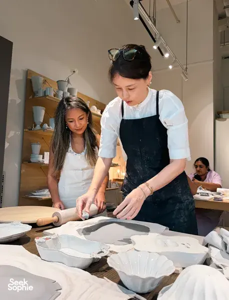 People shaping European-style ceramic plates from clay on a shared table during a Singapore ceramics workshop in studio light