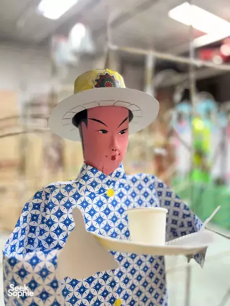 Close-up of a blue-and-white patterned paper deity figure wearing a hat and holding an offering tray in Singapore