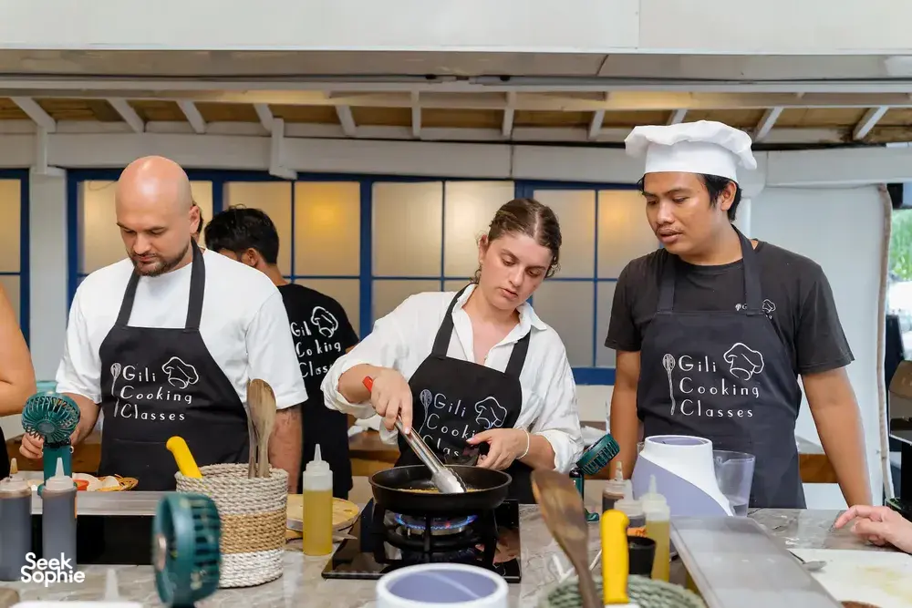 Gili Islands cooking class in Lombok: instructors guide guests at a wok station, preparing Indonesian dishes and peanut sauce
