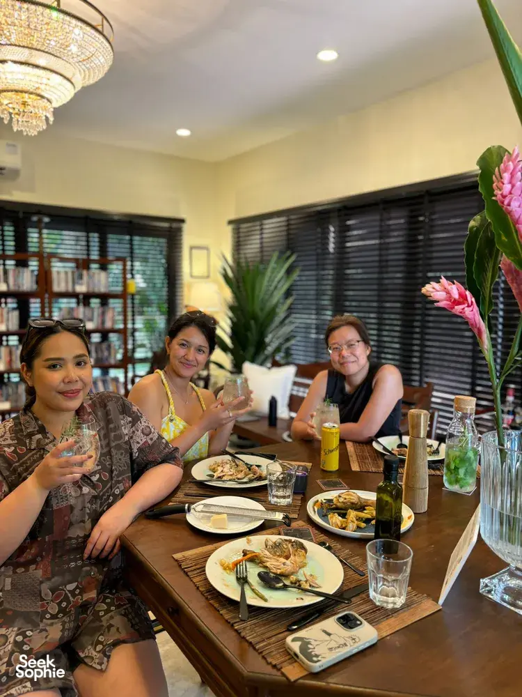 Friends dining around a wooden table with plates and drinks in a warm farmstay home during a 2D1N trip—Singapore hidden gems