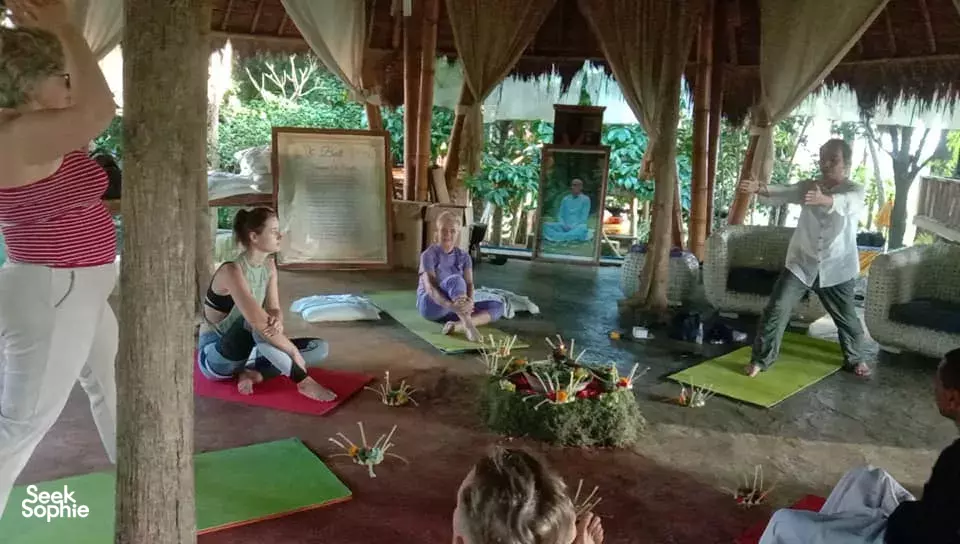 Meditation circle under a pavilion at Omunity Bali in Bali, with participants seated on mats beside flower-and-incense offerings