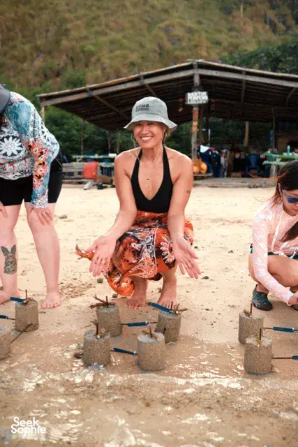 Squatting participant sets coral plugs into concrete bases on a beach restoration site with Rinca Coral Nursery Program in Labuan Bajo