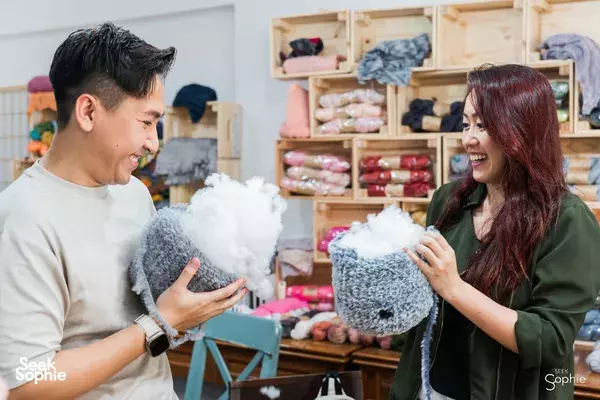 People at Tiny Rabbit Hole Singapore hold fluffy grey plush creations beside yarn shelves — workshops in Singapore