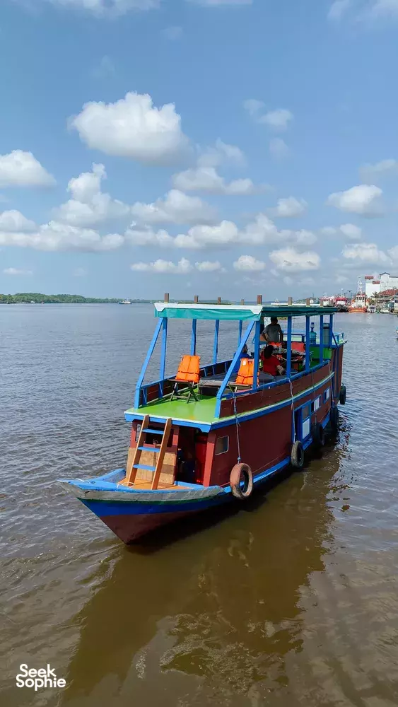 Tanjung Puting small boat cruise on a river, Sister Tour vessel with orange life jackets and passengers near Pangkalan Bun