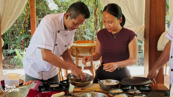 Local chef teaching a participant to cook vegan Manggarai dishes at a shared worktable in Labuan Bajo