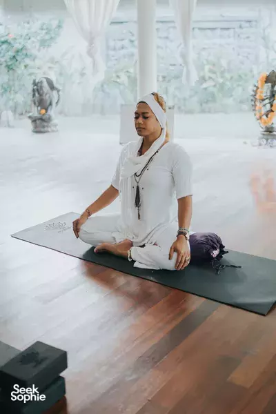 Woman in a meditation pose on a yoga mat in a bright indoor studio in Indonesia, seated in calm yoga posture