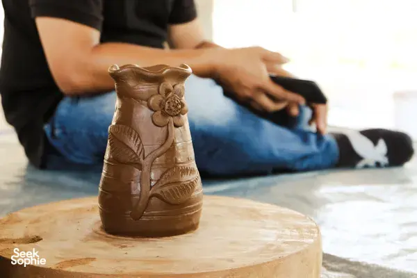 Carved terracotta jug standing on a wooden round block as hands shape and smooth it during pottery in Yogyakarta