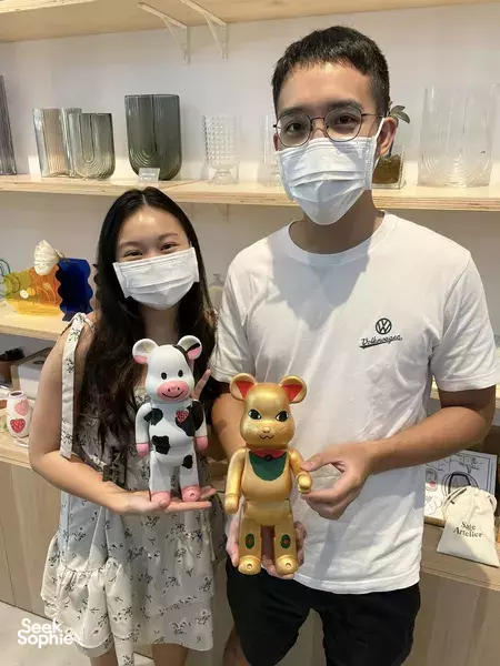 Two masked visitors holding painted bearbrick figures in a bright studio, made during a paint-your-own session in Singapore