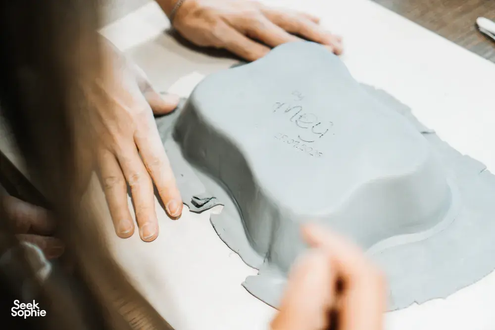 Close-up of hands carving and detailing a grey clay plate with sculpting tools during a Singapore pottery class at the workbench