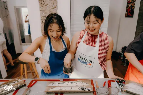 Participants in aprons preparing French baguettes, sprinkling herbs on dough with a jar at French Cooking Lab workshops in Singapore