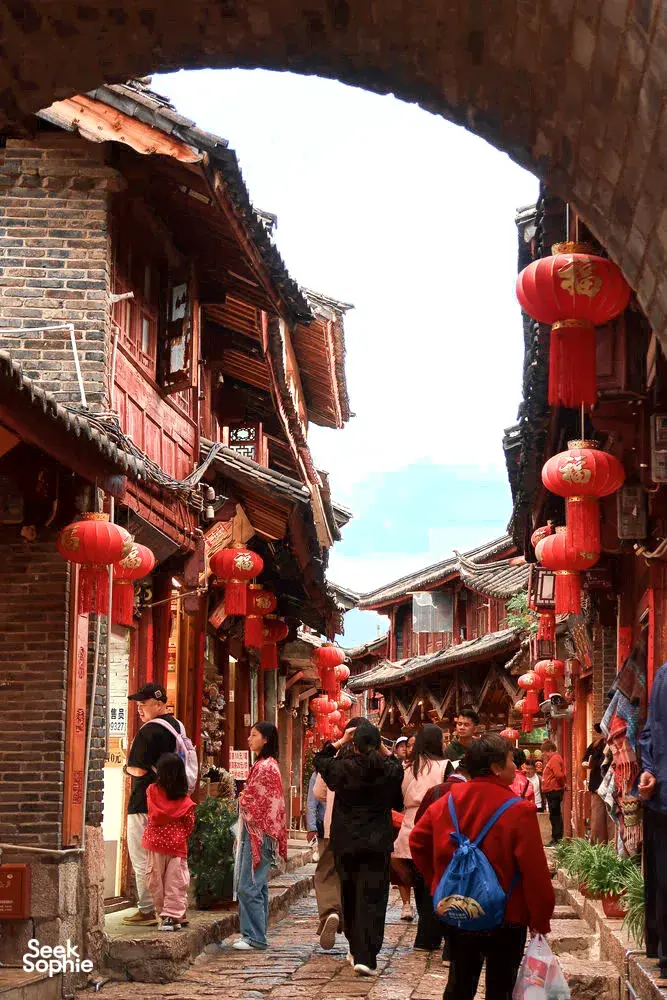 Busy narrow street in Lijiang’s old town with red lanterns and wooden facades as visitors walk through the cobbled lane