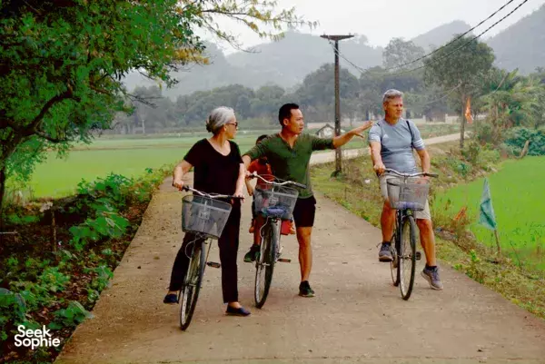 Cyclists riding a quiet country road past rice paddies and karst hills in Ninh Binh during a slow homestay visit