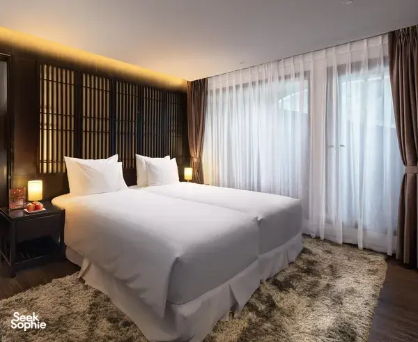 Oasis Bay Party Cruiser cabin with a made-up double bed, bedside lamps and sheer curtains, Halong Bay