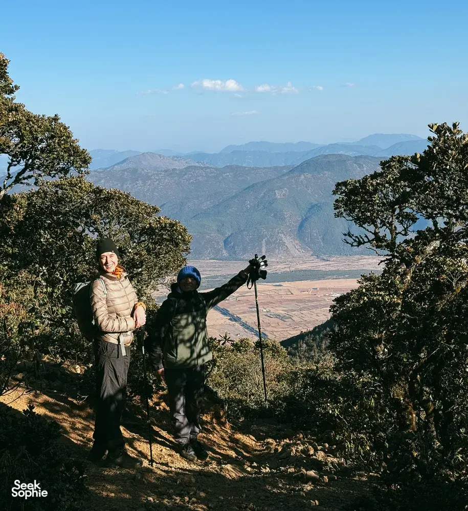 Hikers with trekking poles on a forest trail above Lijiang during a guided hike to the 1st Peak of Jade Dragon Snow Mountain