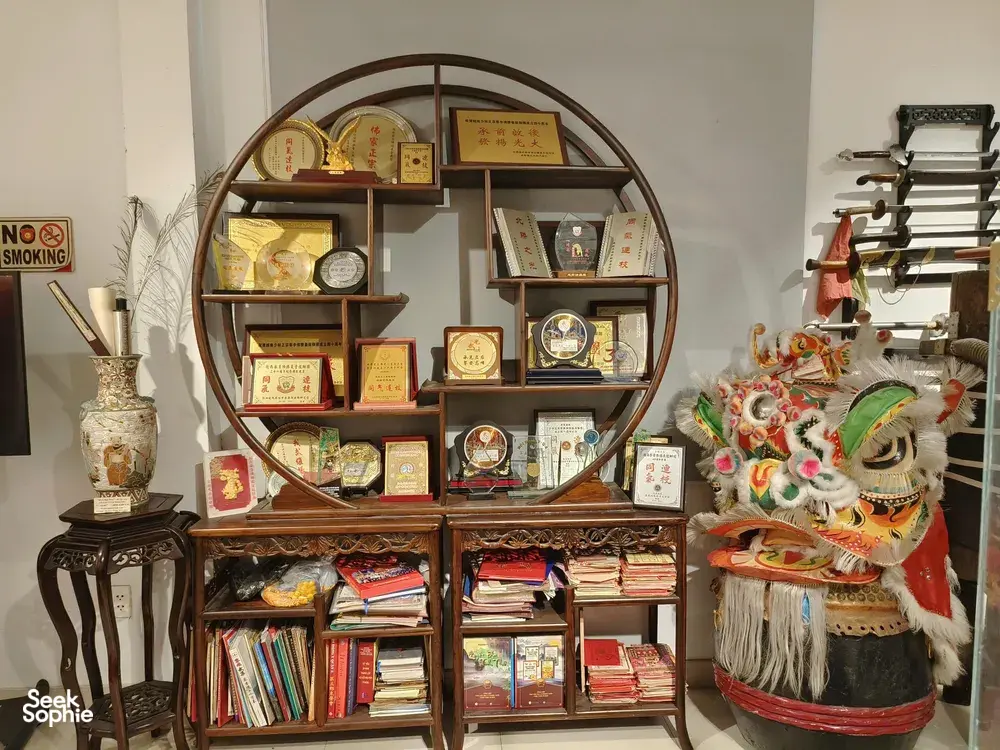 Ho Chi Minh City Chinatown lion-dance museum shelf showing awards, books and a decorated lion mask in a display case