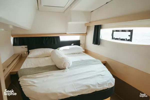 Aquaholic catamaran cabin bedroom with neatly made double bed and pillows, daylight through a window over open water in Singapore