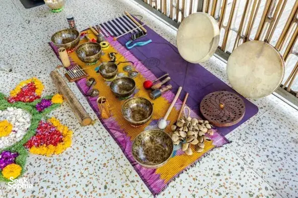 Assortment of brass singing bowls, chimes and mallets on a purple mat with flower petals, ready for sound healing in Canggu