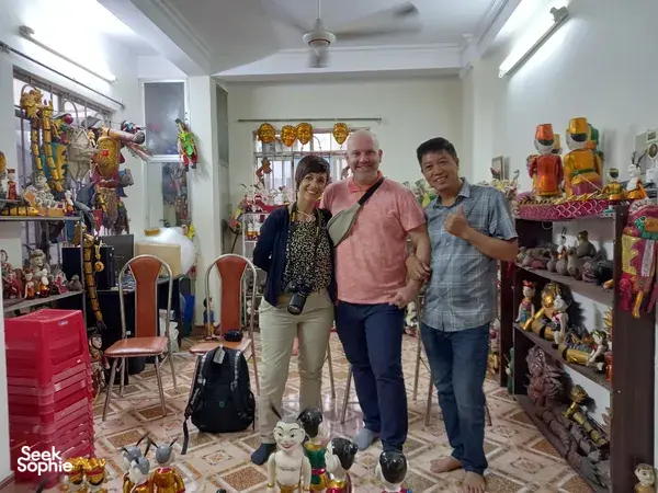 Para pengunjung berpose di ruang lokakarya penuh boneka di Hanoi, dikelilingi boneka air berwarna-warni dan figur panggung sebelum pertunjukan dimulai