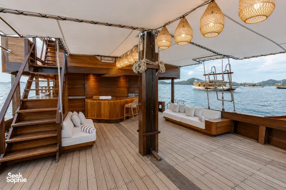 Enclosed wooden deck of a Travass Life phinisi with cushioned lounge seats and hanging lanterns, part of a rare 3D2N trip to Komodo Island