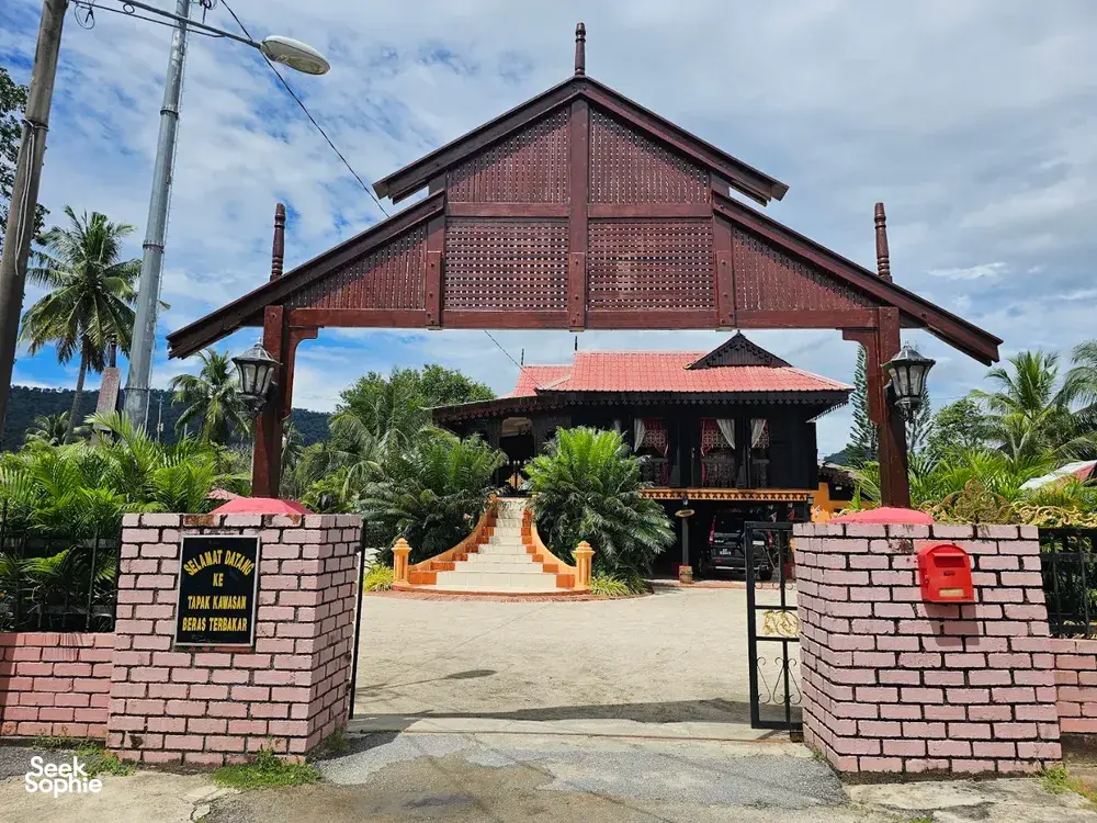 Entrance gate to a traditional building with red roof on Langkawi, viewed from the road during a cycling stop with Dev's Adventure Tours