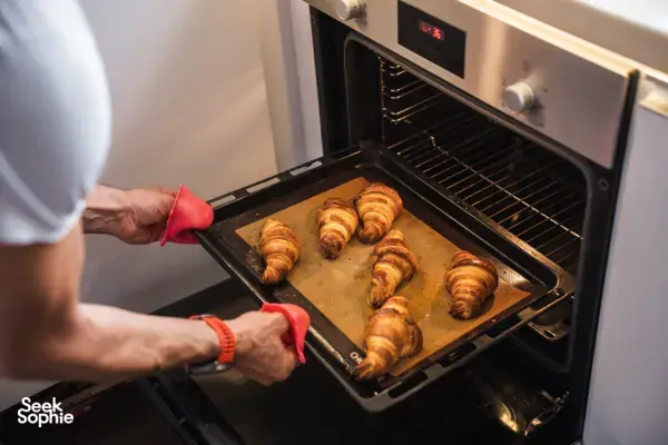 Hands in red oven gloves sliding a tray of croissants out of the oven at French Cooking Lab in Singapore