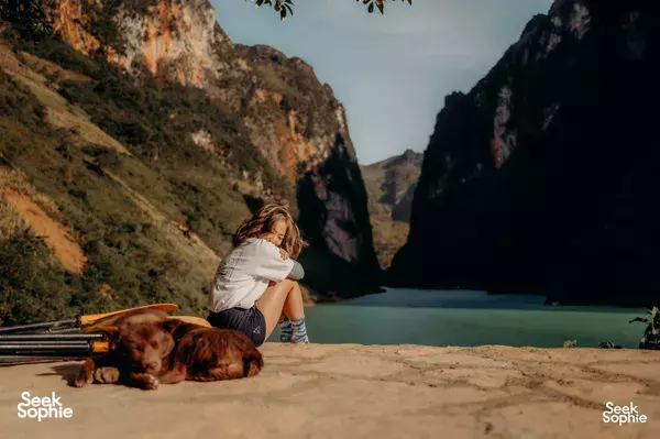 Travellers taking a break on a cliffside stop during a motorcycle tour in Vietnam, with a woman and her dog in the valley