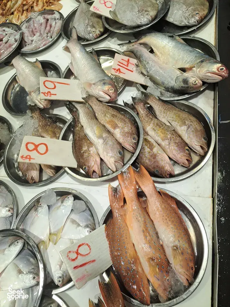 Pelbagai ikan segar seekor-seekor di atas dulang logam di pasar makanan laut Singapura, setiap satunya dengan tanda harga tulisan tangan untuk pembeli