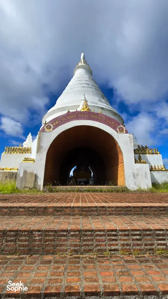 White stupa doorway under dramatic clouds with gold details beside a brick courtyard in Khao Sok National Park
