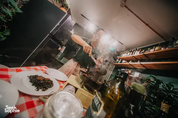 Chef cooking at a stove in Singapore, steam rising as appetisers sizzle beside herbs for private dining Singapore