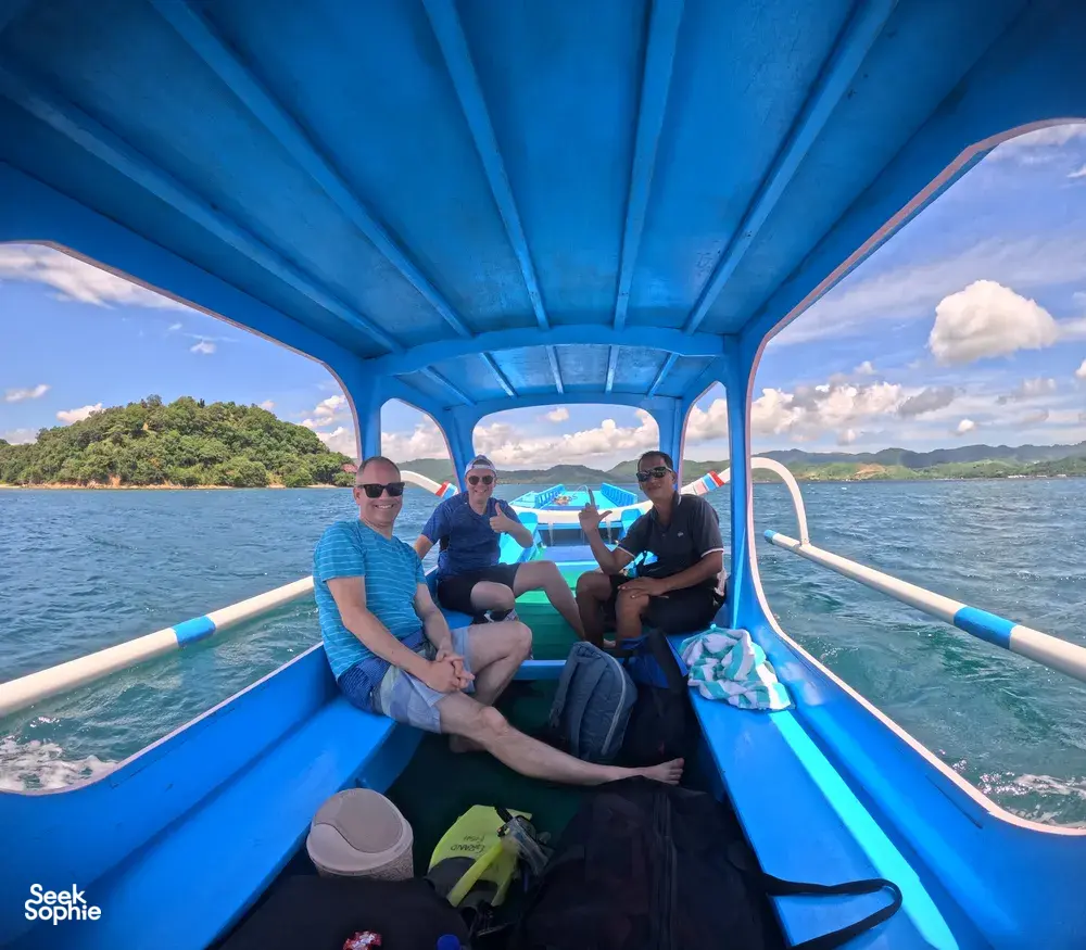 Para penumpang tersenyum dan melambai di atas bot bermotor biru dalam perjalanan ke Kepulauan Gili untuk aktiviti snorkeling persendirian berhampiran Lombok