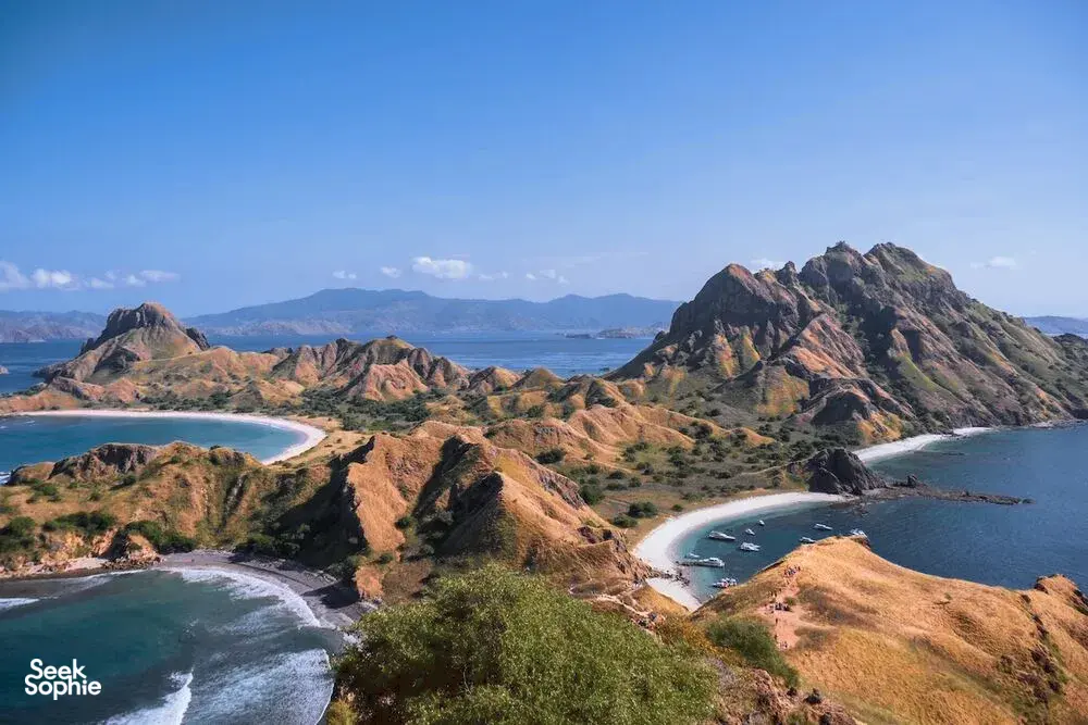 Aerial view of rugged hills, winding beaches, and teal waves along the coast in warm late-afternoon light, around Labuan Bajo