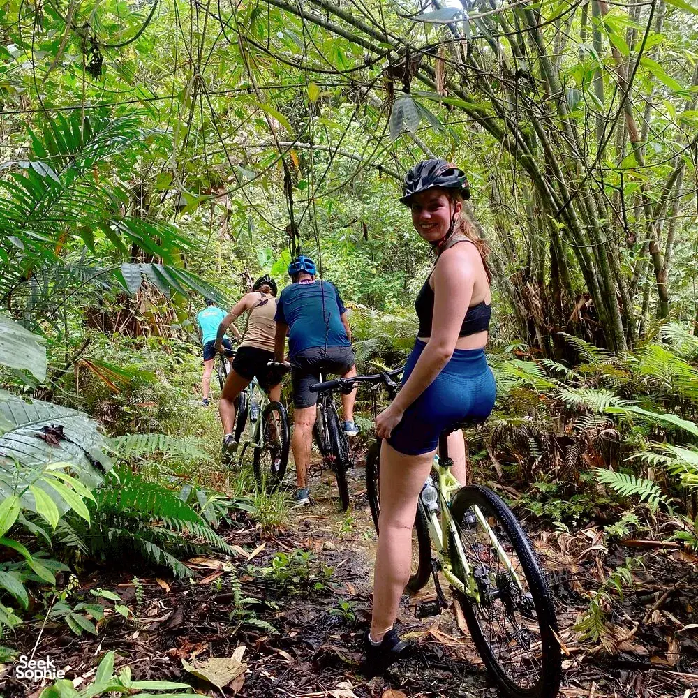 Cyclists on mountain bikes riding a muddy jungle trail near Kuching with Paradesa Borneo on an adventure cycling tour