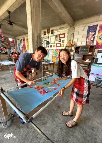 Batik workshop at Five Arts Studio in Keliki, two people paint colourful motifs on fabric stretched on a batik frame in Ubud