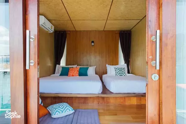Glamping room interior with two neatly made beds, wooden walls and open doors leading to the lake view in Khao Sok