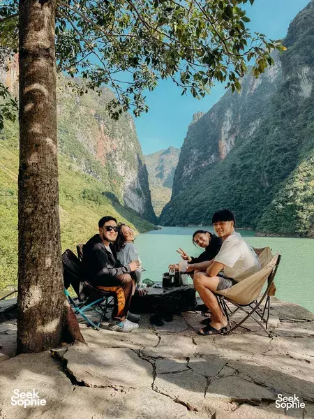 Picnic lunch on a riverside ledge during a motorcycle tour in Vietnam, with travellers relaxing in front of steep mountain walls